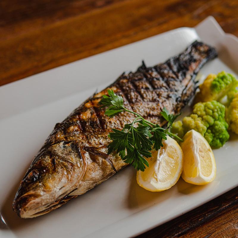 Whole grilled fish with lemon wedges and vegetables