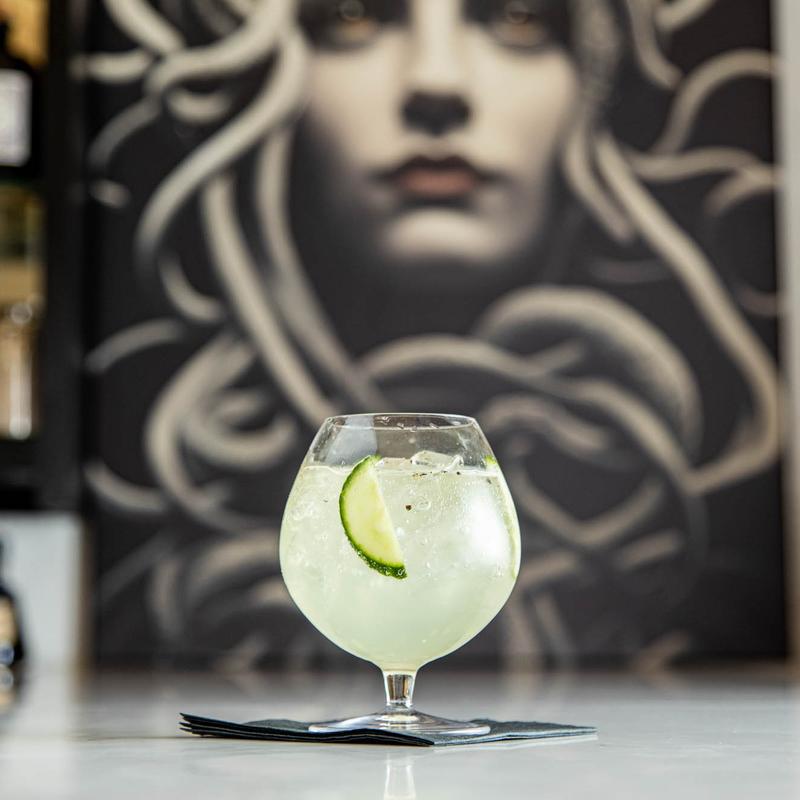 Pale green cocktail with a lime slice beside wall art