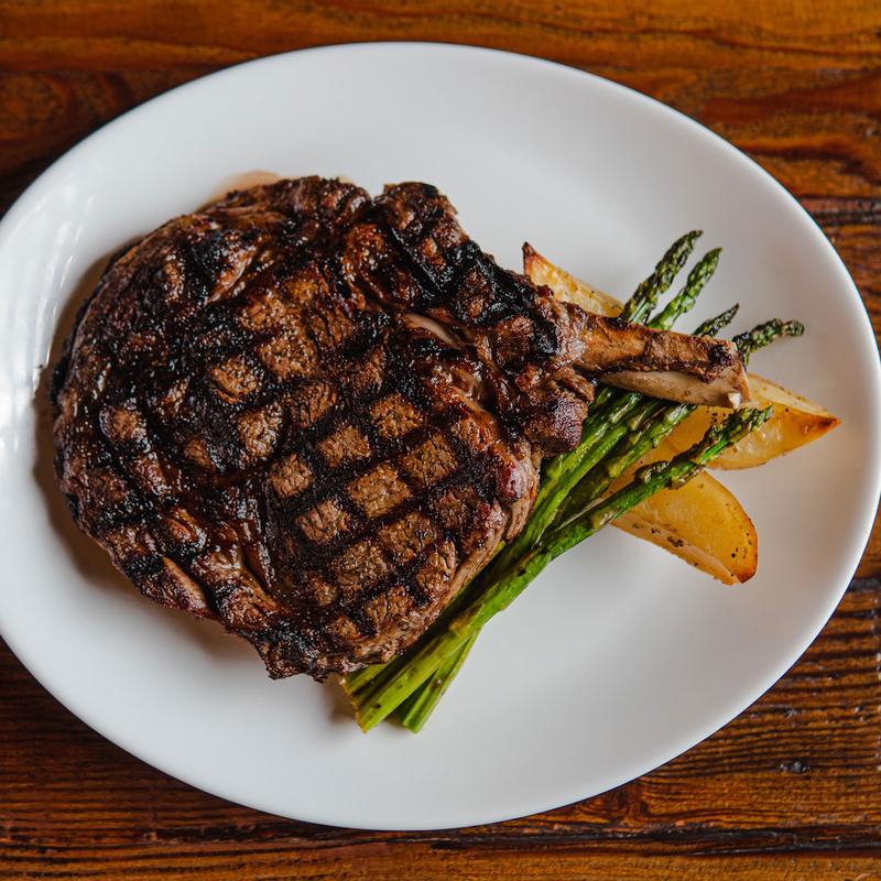 Grilled bone-in steak and vegetables on a white plate